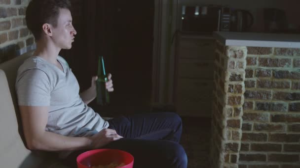 Man, football fan is drinking beer and chips in front of TV - Footage, Video