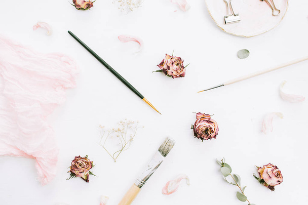 Composición de boda creativa con flores de rosas, ramas de eucalipto y pinceles sobre fondo blanco. Plano laico, vista superior elegante concepto de arte
. - Foto, imagen