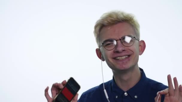 Young handsome man singing, dancing, listening music in headphones over white background - Felvétel, videó