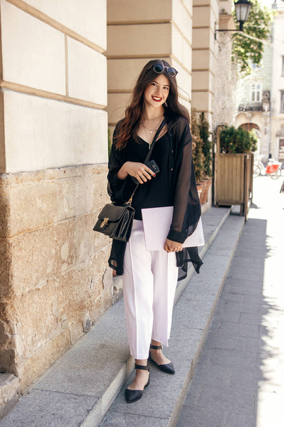 happy stylish brunette businesswoman standing with notebook on city street, full length - Fotografie, Obrázek