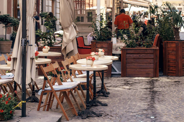 beautiful cafe terrace with little vintage tables and wooden chairs and plants, modern exterior of restaurant in european city street. food court in old city - Photo, Image