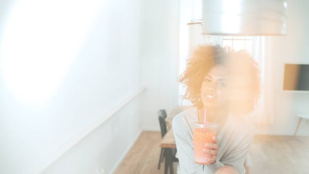Happy mixed race woman holding smoothie, looking to camera. - Photo, Image