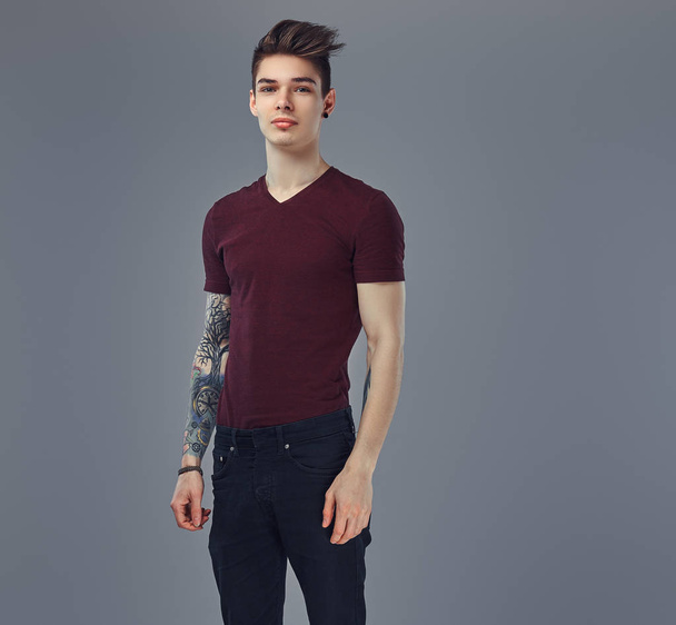 Handsome fashionable young guy with stylish hair and tattoo on his arm posing in a studio. - Photo, Image