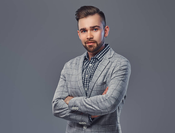 Handsome bearded man with hairstyle in an elegant gray jacket, posing with crossed arms in a studio, looking at a camera. - Photo, Image