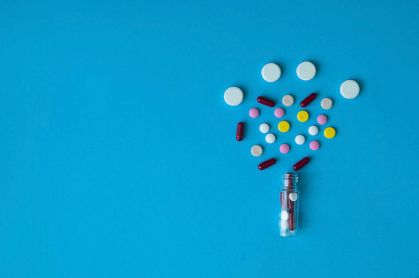 pastillas de color, cápsulas, vitaminas que vuelan fuera de un vial sobre un fondo azul, concepto de vida, primer plano
 - Foto, imagen