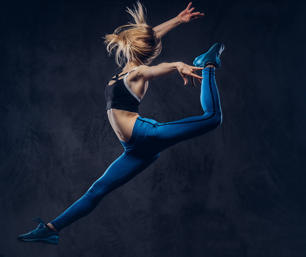 Giovane ballerina bionda in balli di abbigliamento sportivo e salta in uno studio. Isolato su uno sfondo scuro
. - Foto, immagini