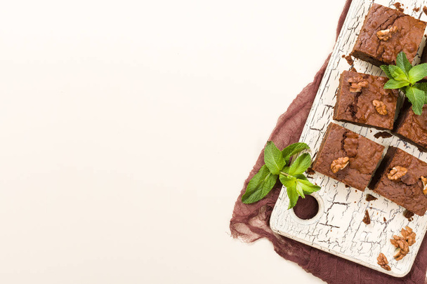 Brownie sweet chocolate dessert with walnuts and meant leaves on retro board with copy space on pastel beige background. Beautiful banner with delicious brown cocoa baked pastry. - Photo, image