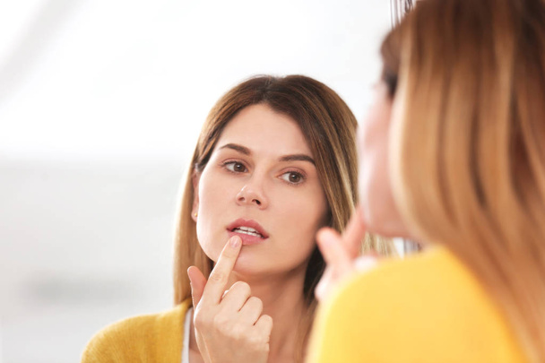 Kobieta z nałożeniem kremu opryszczki na ustach przed lustrem - Zdjęcie, obraz