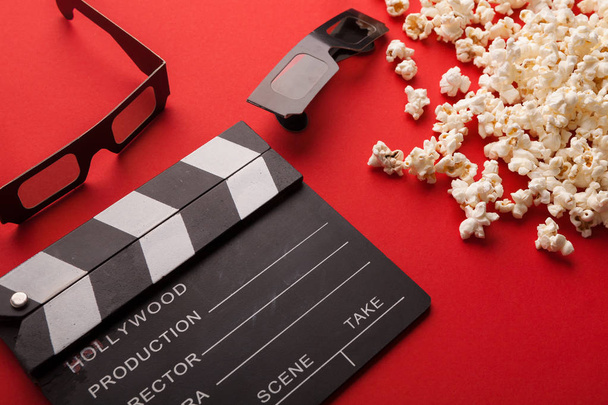 Clapperboard, 3D glasses and popcorn on red background - Photo, Image