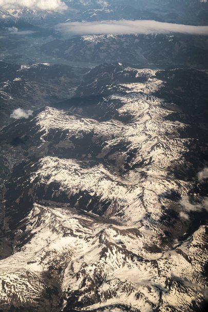 Vista hacia abajo en la cima de la cordillera de los Alpes europeos con gorras de nieve y nubes blancas y esponjosas flotando sobre un avión
. - Foto, Imagen