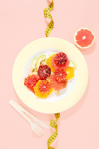 Healthy dietary fruit salad made of oranges, grapefruit and avocado on pink background with measuring tape. Top view, flat lay. Healthy and dietary food concept - Фото, зображення