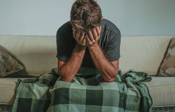 young sad and desperate man at home sitting at living sofa couch covering face with hands crying suffering depression and stress feeling miserable in sadness anxiety and lifestyle concept - Fotoğraf, Görsel