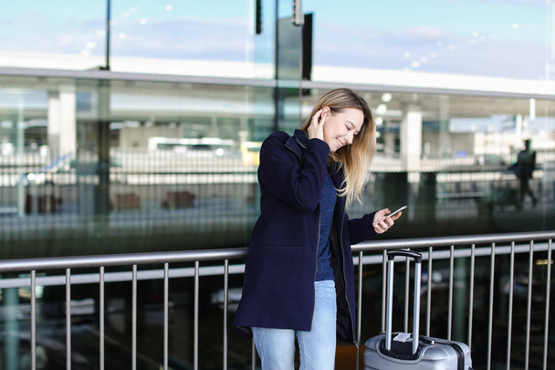 Woman staying with smartphone and valise near airport. - Fotoğraf, Görsel