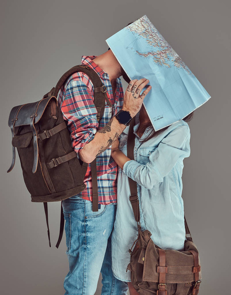 Atractiva pareja de turistas besándose mientras se cubren la cara con un mapa, acurrucándose en un estudio
. - Foto, Imagen
