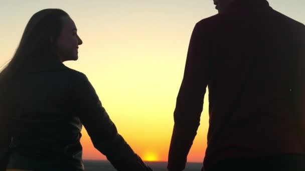 Feliz pareja joven tomados de la mano mirando el uno al otro en el increíble atardecer al aire libre
 - Metraje, vídeo