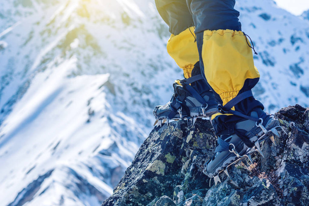 アイゼンのクライマーは、雪山の背景にピークに入り口の前で岩の上立っています。足をクローズ アップ。旅行パスと目標を達成するための概念 - 写真・画像