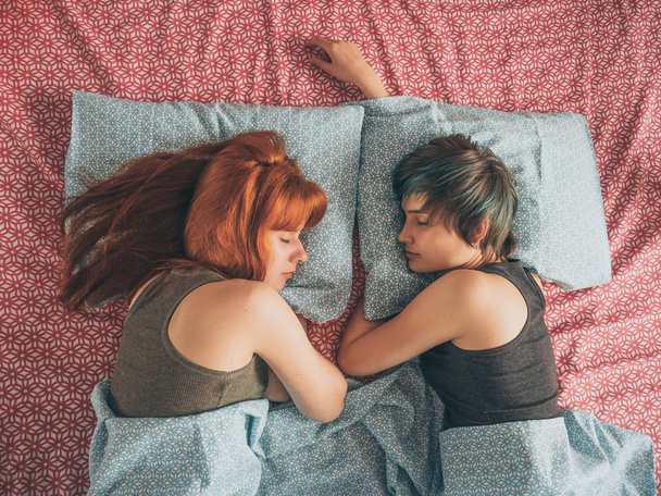 Жінки лежать на ліжку, молоді лесбіянки цілуються і обіймаються
 - Фото, зображення