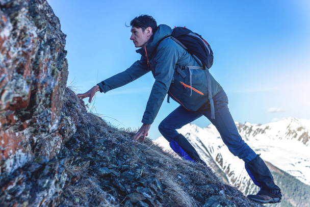 Homem Caminhadas com uma mochila rastejando sobre rochas rochosas para o topo no fundo de montanhas nevadas. Conceber a maneira difícil e meta de realização
 - Foto, Imagem