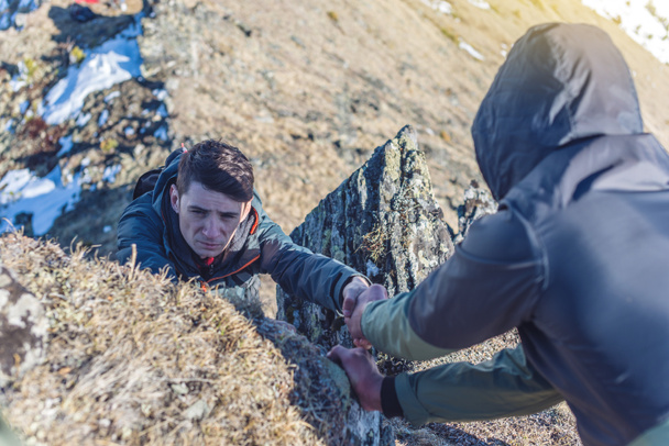 Um homem ajuda o amigo a subir ao topo. Caminhante dá uma mão para puxar o na montanha
. - Foto, Imagem