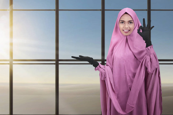 Mooie Aziatische Moslimvrouw tonen copyspace gebied met glas achtergrond van venster - Foto, afbeelding