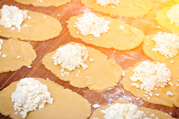 Eine Großaufnahme einer Bäckerin in Schutzhandschuhen zieht den Teig zum Kochen von Semmeln mit Käse auf einem geknoteten Tisch mit einem Nudelholz heraus. - Foto, Bild