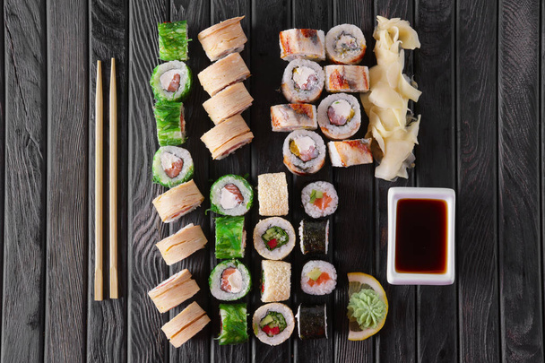 Large set of rolls with garnish and hashi on wooden plate - Foto, Imagen