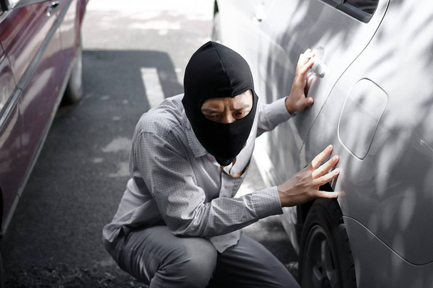 Masked burglar wearing a balaclava ready to burglary against car background. Insurance crime concept. - Photo, Image