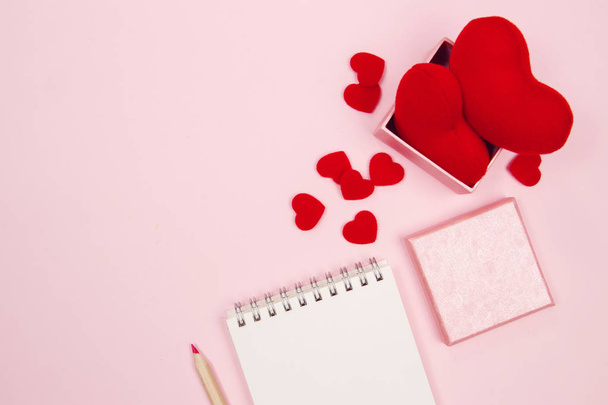 Espacio de trabajo femenino con cuaderno en blanco, caja de regalo y corazón rojo sobre fondo rosa con espacio para copiar. Acostado. Vista superior
.  - Foto, Imagen