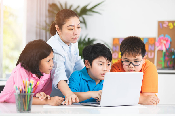 Asyalı kadın öğretmen ve şirin Asyalı çocuklar birlikte dizüstü bilgisayar kullanan. - Fotoğraf, Görsel
