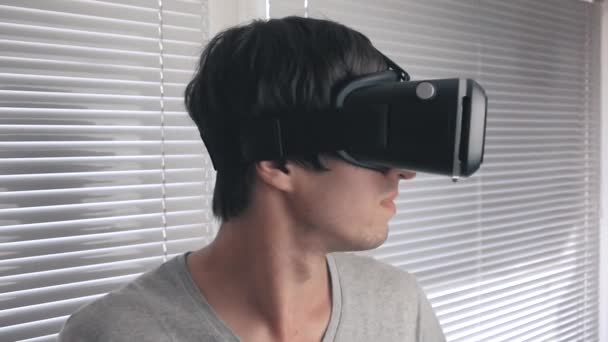 Молодой человек использует свою VR гарнитуру для просмотра 360 видео на офисном фоне. Закрыть
. - Кадры, видео