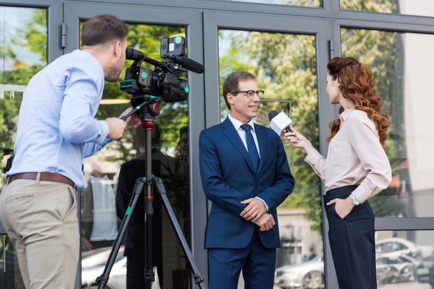 cameraman e news anchor intervistando uomo d'affari vicino edificio per uffici
  - Foto, immagini