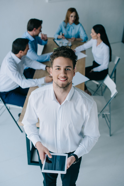 selective focus of smiling businessman and coworkers at workplace in office - Photo, Image