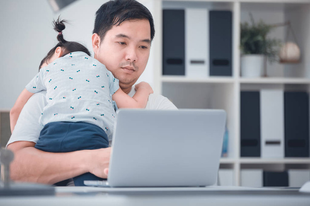asiatische moderne Familie und kleines Mädchen, während Papa mit Notizbuch auf dem Arbeitstisch im Home Office arbeitet.  - Foto, Bild