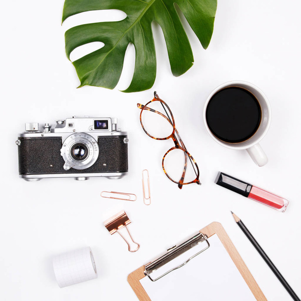 Women's home office desk workspace with tropical palm leaf, vintage camera, glasses, coffee cup, lipstick and notebook on white background. Flat lay, top view woman blog mock up. Creative concept. - Photo, Image