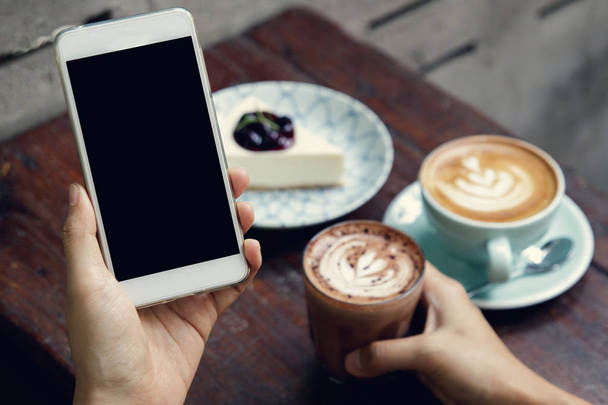 Крупним планом зображення жінки або чоловічих рук за допомогою смартфона в кафе під час пиття кави. Введення текстового повідомлення через мобільний телефон, концепція соціальних мереж. Макет смартфона
. - Фото, зображення