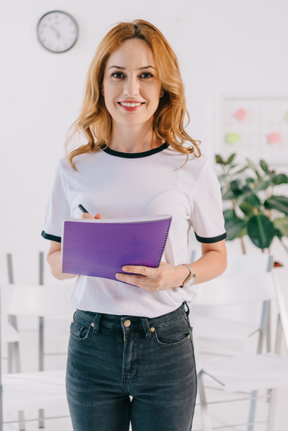 portrait of smiling businesswoman in casual clothing with notebook in hands, business training concept - Фото, изображение