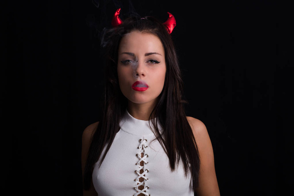 Młoda kobieta z diabeł rogi na głowie i dym papierosowy pozowanie na czarnym tle - Zdjęcie, obraz