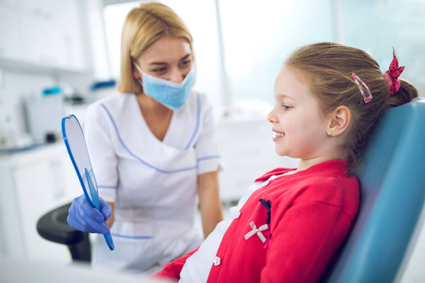 Female dentist shows little girl how to appearanc - Valokuva, kuva