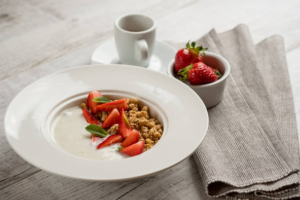 close-up photo of healthy oatmeal with fresh strawberries and green mint leaves with milk in white plate on grey wooden table - Фото, зображення