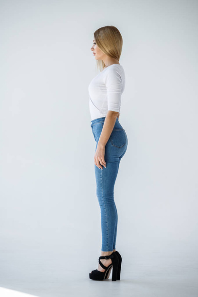 Studio shot of lovely blonde girl in white shirt and blue jeans standing on white background - Foto, afbeelding