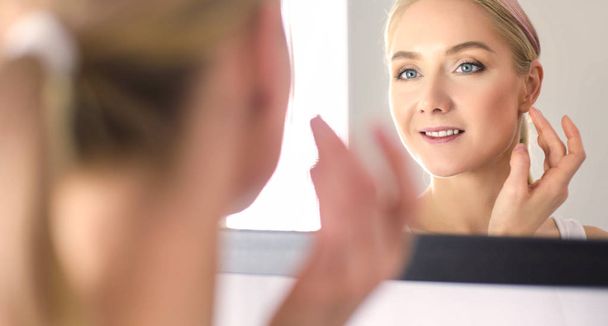 Woman caring of her beautiful skin on the face standing near mirror - Foto, Bild