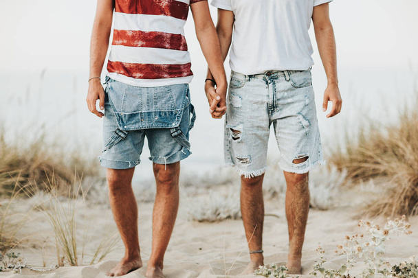 Two male friends holding hand together on sandy beach  - Фото, зображення