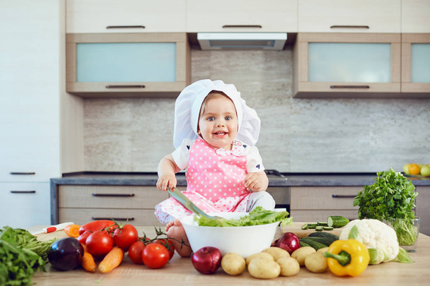 A little girl in a chefs hat prepares in the kitchen. - 写真・画像
