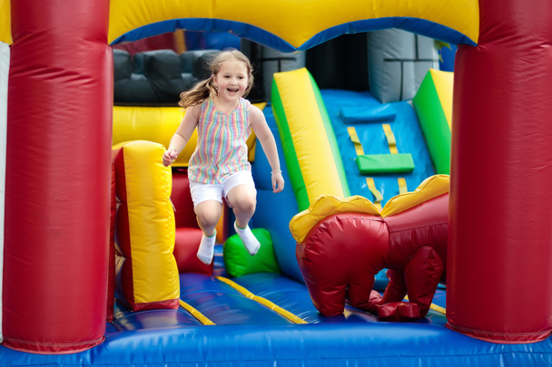 Child jumping on colorful playground trampoline. Kids jump in inflatable bounce castle on kindergarten birthday party Activity and play center for young child. Little girl playing outdoors in summer. - Photo, Image