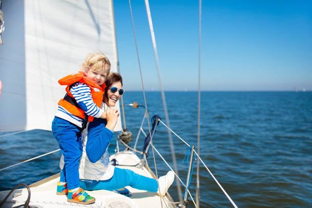 Mother and baby boy sail on yacht in sea. Family sailing on boat. Mom and kid in safe life jacket travel on ocean ship. Parent and child enjoy yachting cruise. Summer vacation. Sailor on sailboat. - Foto, afbeelding