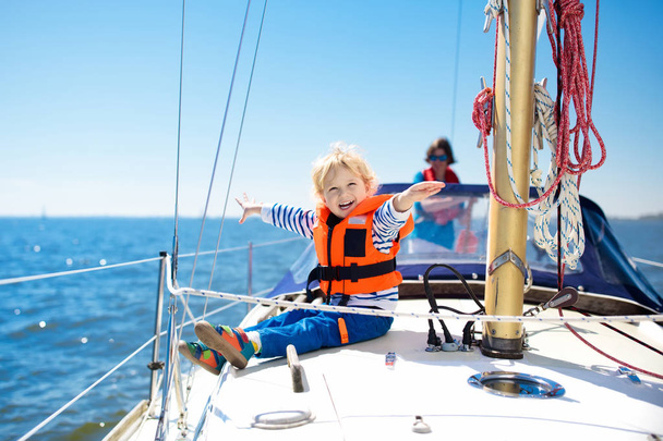 Τα παιδιά ταξιδεύουν με γιοτ στη θάλασσα. Παιδί που πλέει με πλοίο. Ένα μικρό αγόρι με ασφαλή σωσίβια ταξιδεύει με πλοίο των ωκεανών. Τα παιδιά απολαμβάνουν κρουαζιέρα με γιοτ. Καλοκαιρινές διακοπές για οικογένεια. Νεαρός ναύτης στο μπροστινό κατάστρωμα ιστιοφόρου. - Φωτογραφία, εικόνα