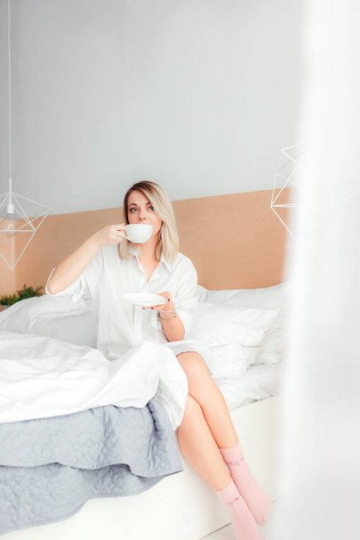 Beautiful woman drinking a coffee sitting on her bed home - Fotoğraf, Görsel
