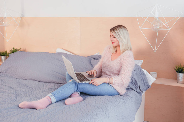 Счастливая случайная красавица, работающая на ноутбуке, сидящая на кровати в хоусе
 - Фото, изображение