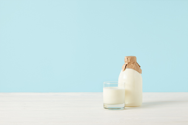 pohár tej és a tej-palack csomagolva papírt a kék háttér  - Fotó, kép