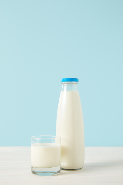 Close-up beeld van fles melk en melkglas op blauwe achtergrond  - Foto, afbeelding